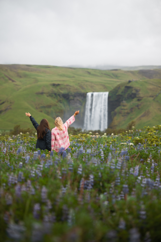 Deux femmes se tiennent dans un champ de lupins devant la cascade Skogafoss en Islande