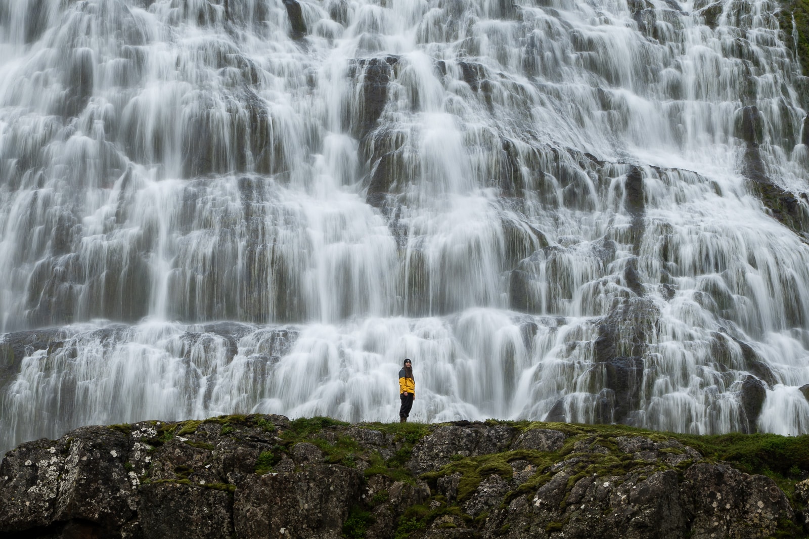 Une femme se tient devant une cascade immense en Islande