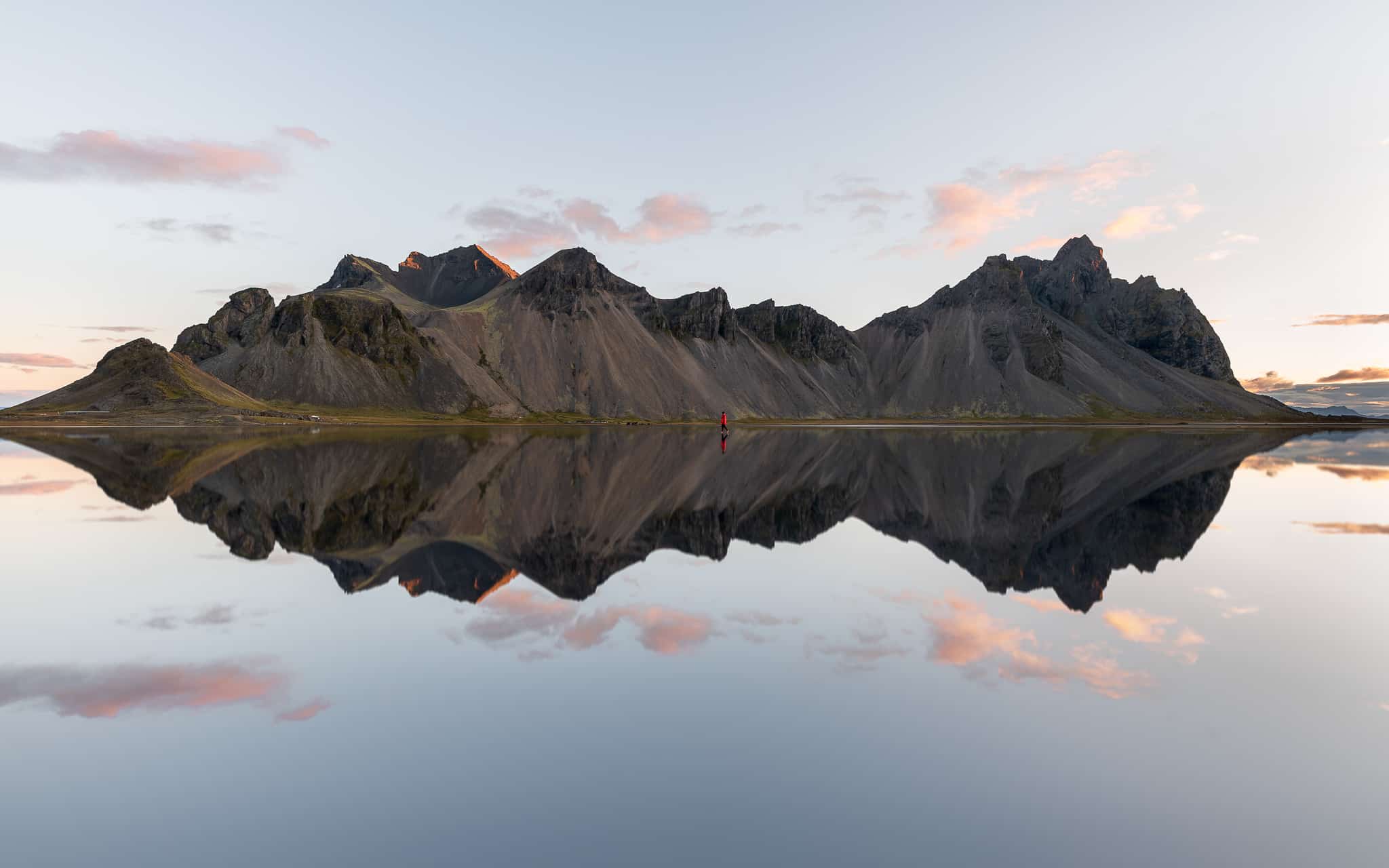Femme marchant dans l'eau devant une montagne islandaise qui se reflète au lever du soleil