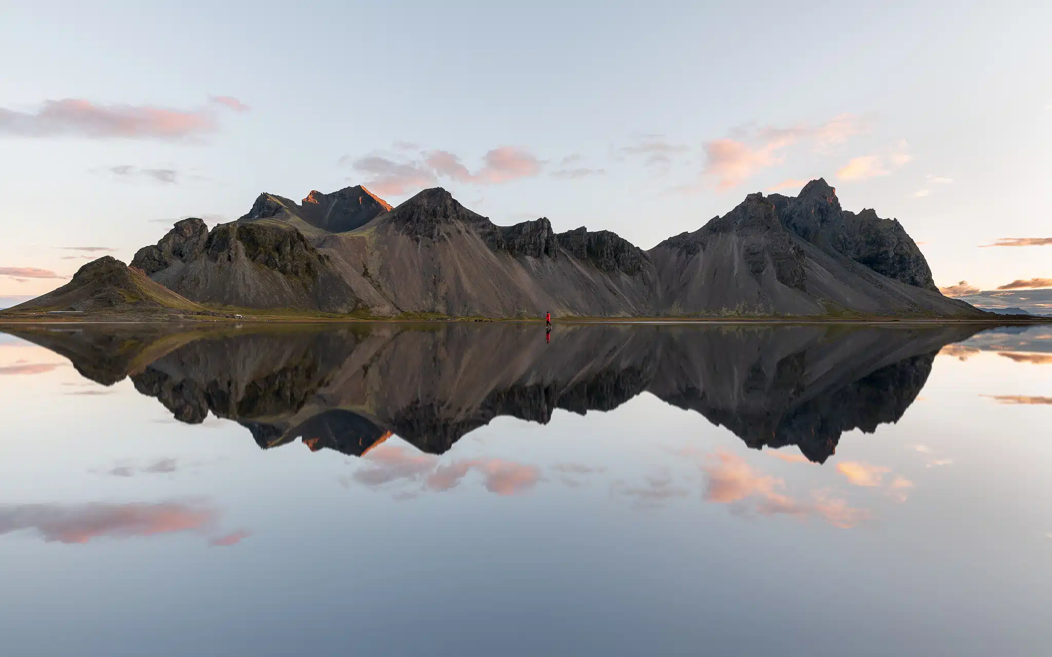 Femme marchant dans l'eau devant une montagne islandaise qui se reflète au lever du soleil