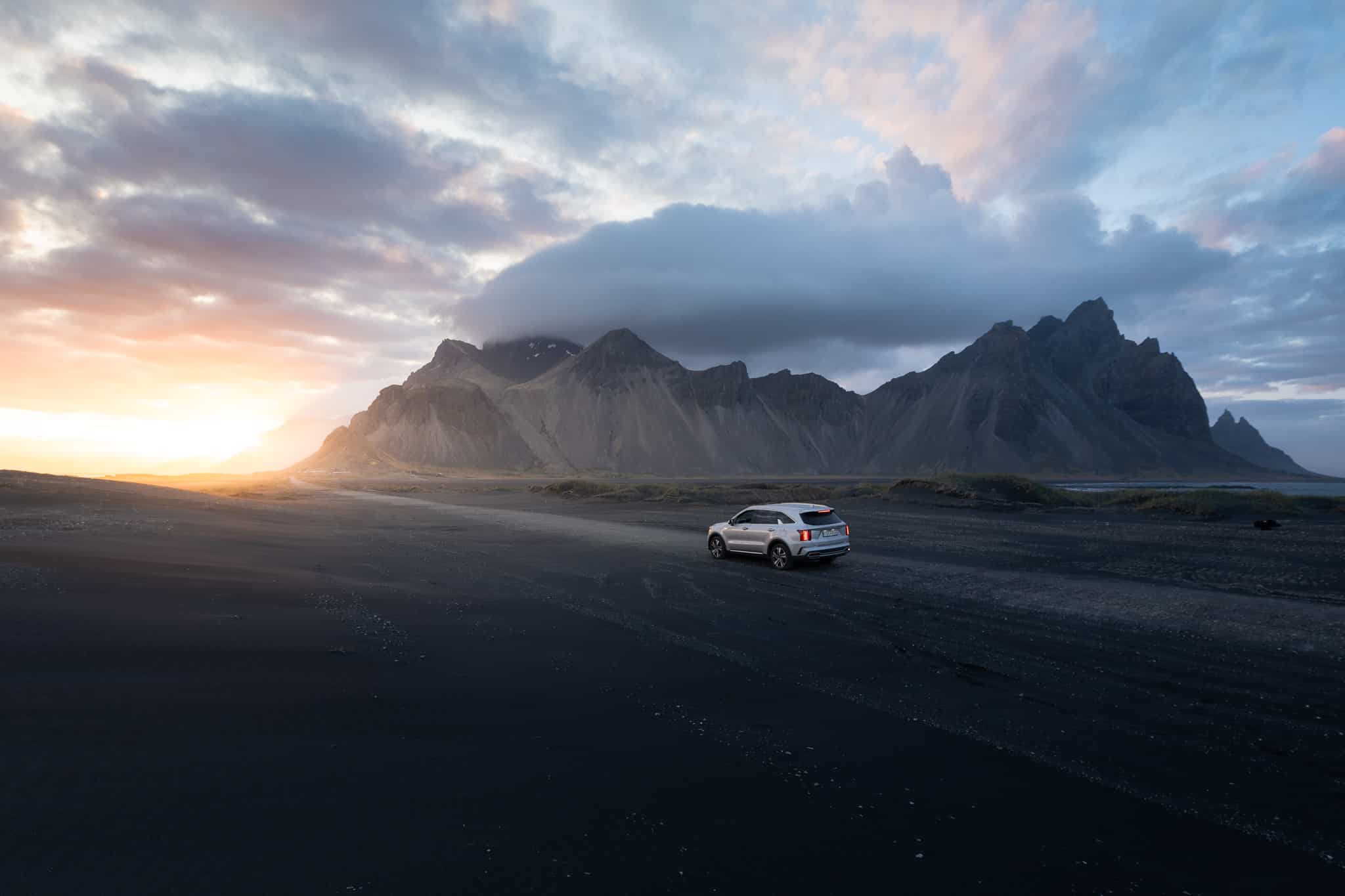 Une voiture roule devant une montagne en Islande au coucher de soleil
