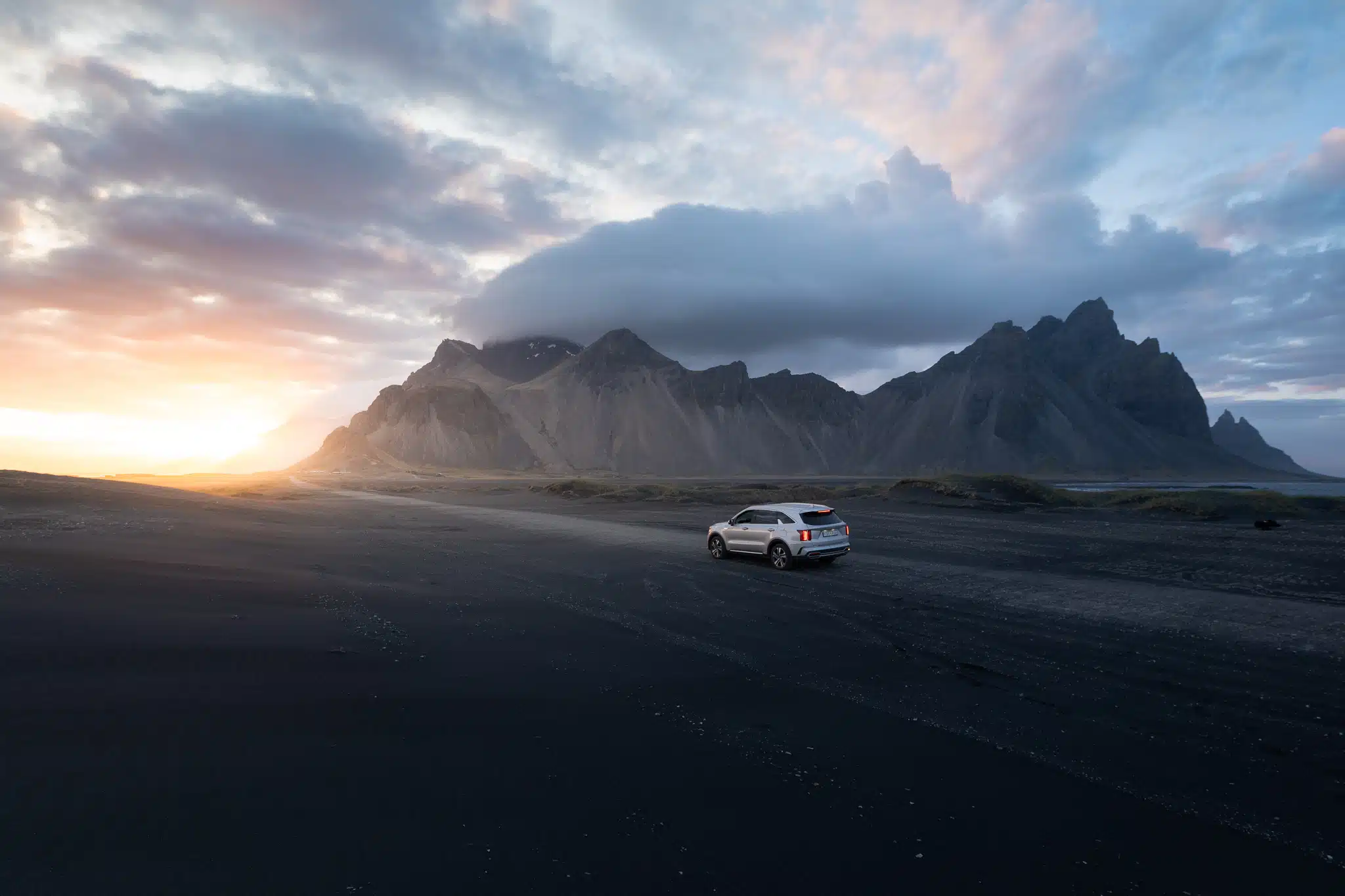 Une voiture roule devant une montagne en Islande au coucher de soleil