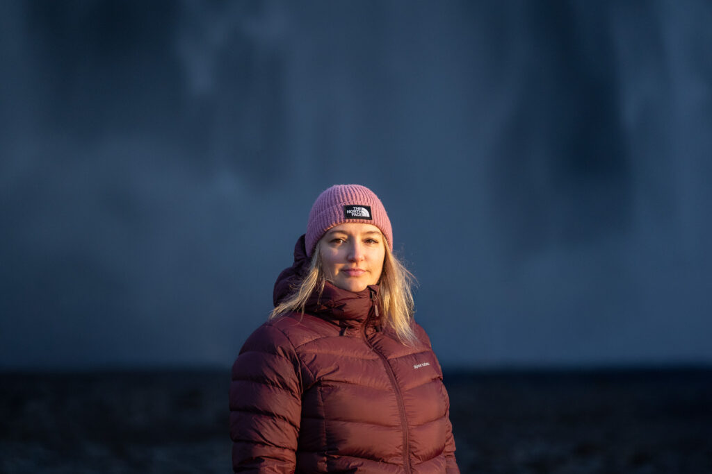 Femme portant un bonnet épais pour se protéger du vent devant une cascade en Islande