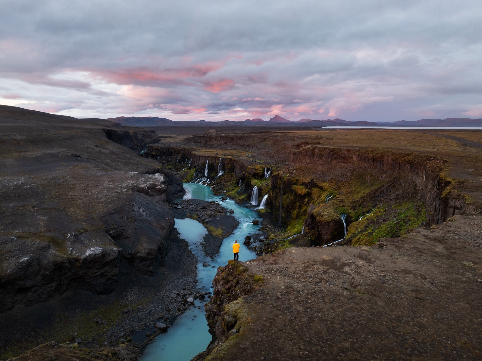 Une femme se tient devant une cascade dans les Hautes-Terres en Islande au coucher de soleil
