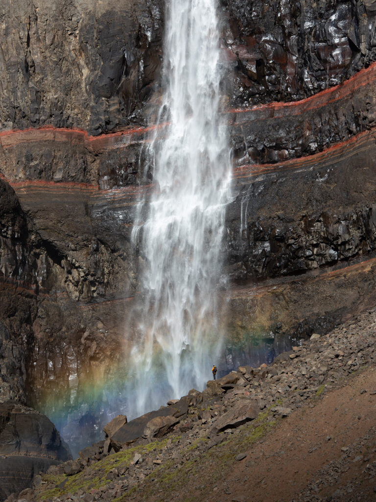 Un homme se tient devant la cascade islandaise de Hengifoss