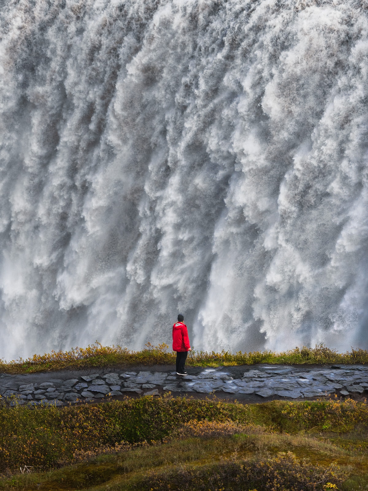 Une femme se tient devant la cascade islandaise Dettifoss