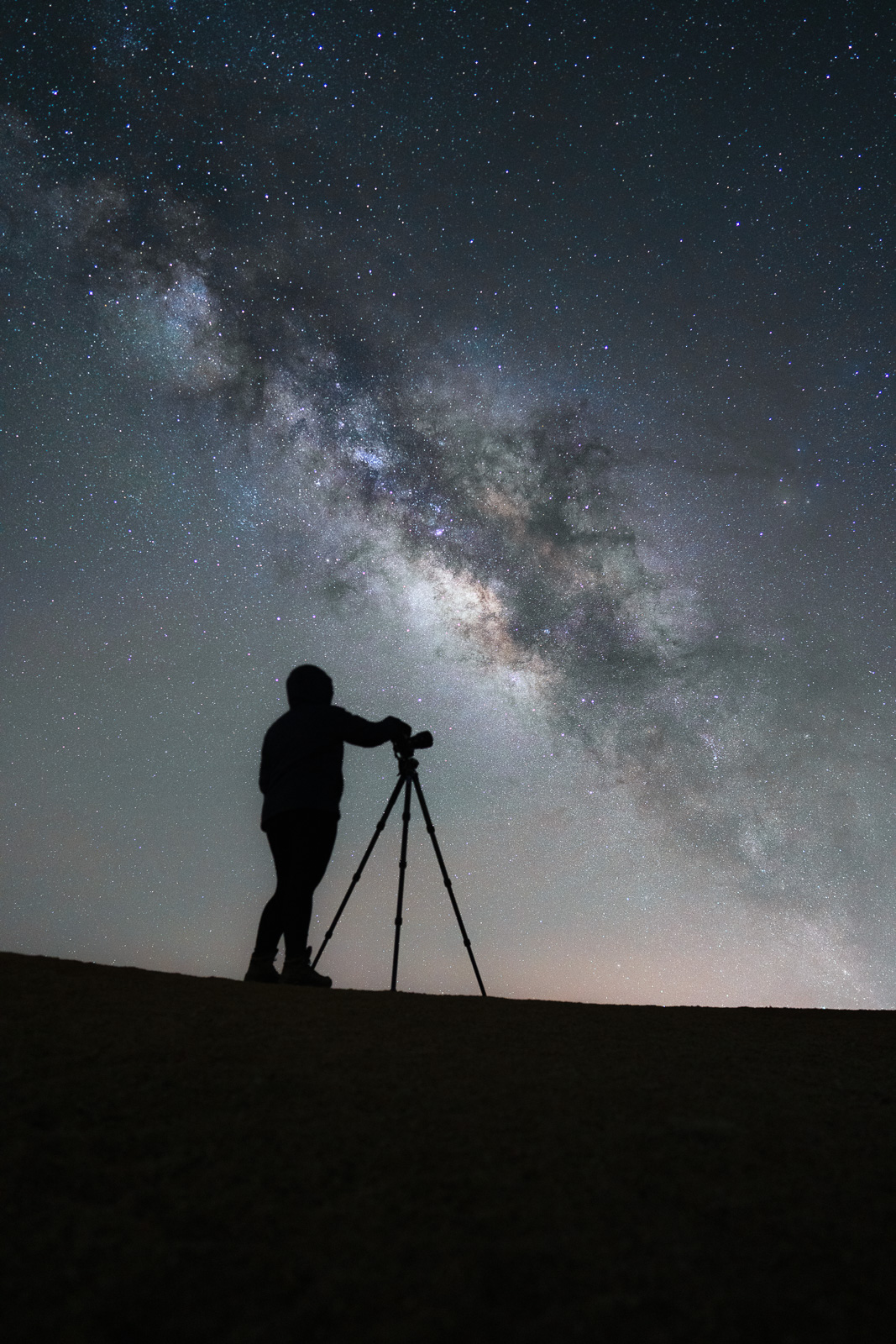 Une femme photographie la Voie lactée grâce un trépied et un appareil photo grand angle